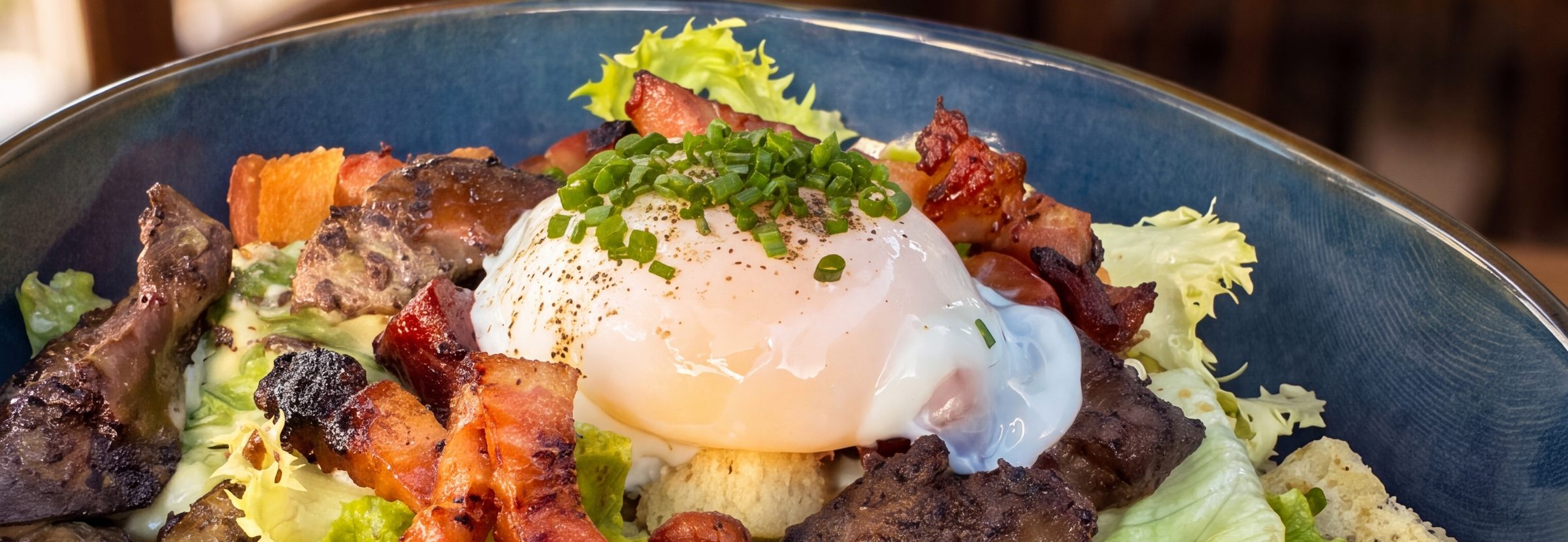 Salade lyonnaise du Clos de l'Abbaye : frisée, lardons, croûtons et œuf poché dans un bol bleu