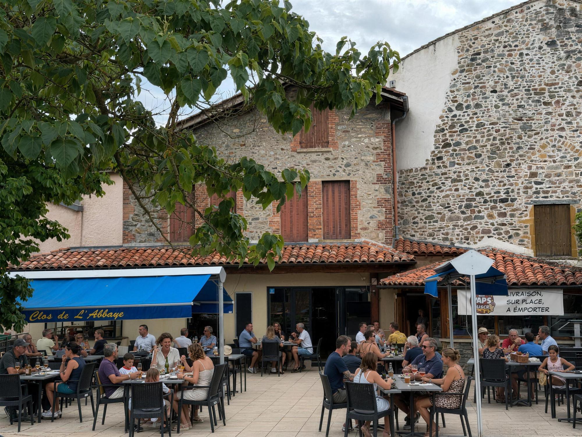 La terrasse du Clos de l'Abbaye un jour d'ete, tables pleines sous le store bleu et le mur de l'abbaye